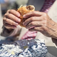 closeup of senior man eating a burger outdoors on a sunny day. - junk food stock pictures, royalty-free photos & images