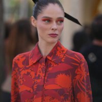 Coco Rocha wears a large hair bow tie, a red and orange floral print jacket, flared pants, outside Akris, during the Womenswear Spring/Summer 2024 as...