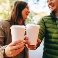 coffee on go during date: woman and man laugh while sipping coffee from biodegradable cups - junk food stock pictures, royalty-free photos & images