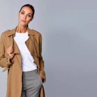 confident young woman holding brown trench coat - fashion stock pictures, royalty-free photos & images