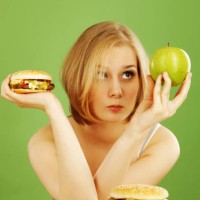 contemplative woman holding apple and hamburger deciding - junk food stock pictures, royalty-free photos & images