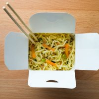 cooked instant noodles, sprinkled with spices, vegetables and herbs, freeze-dried meat. nearby are wooden chopsticks. asian chicken soup with ramen noodles in a paper box, on the dining room kitchen table. the concept of home