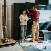 couple discussing over document while fixing cabinet together in kitchen during home renovation - home decoration stock pictures, royalty-free photos & images