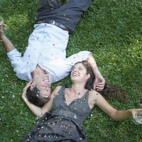 couple outdoors lying on grass with white wine and confetti laughing - garden decoration stock pictures, royalty-free photos & images