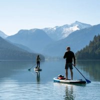 couple paddle sup boards across mountain lake, whistler - travel stock pictures, royalty-free photos & images
