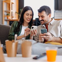 couple relaxing on sofa using smartphones and eating takeaway food - junk food stock pictures, royalty-free photos & images
