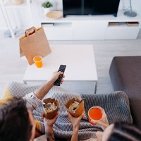 couple relaxing on sofa, watching television and eating takeaway food - junk food stock pictures, royalty-free photos & images