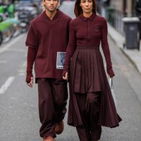 Couple Sebastien Roques wears burgundy shirt, pants & Alice Barbier wears pleated skirt, white bag, zipper outside Lacoste during Womenswear...