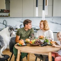 cozy family lunch: middle-aged parents, daughter, and their australian shepherd enjoy a meal together in their warm kitchen. - junk food stock pictures, royalty-free photos & images