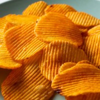 crispy fried potato chips in a bright ceramic bowl or plate, on a white background or table. corn spicy fatty chips with paprika and spices. the concept of unhealthy diet and lifestyle, accumulation of excess weight. copy spa