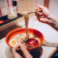 cropped hand of woman eating a bowl of freshly served traditional japanese ramen with chopsticks in a japanese restaurant. asian cuisine and food culture. eating out lifestyle - food stock-fotos und bilder