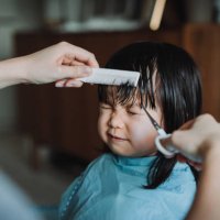cropped hands of young asian mother cutting hair of her little daughter at home - hairstyle stock-fotos und bilder