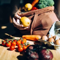 cropped shot of asian woman coming home from grocery shopping, shopping for fresh and healthy organic fruits and vegetables with a reusable shopping bag. unpacking groceries over the kitchen counter. responsible shopping. zer