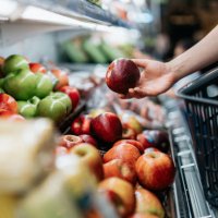 cropped shot of young asian woman choosing fresh organic fruits in supermarket. she is picking a red apple along the produce aisle. routine grocery shopping. healthy living and eating lifestyle - food stock pictures, royalty-