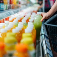 cropped shot of young asian woman shopping for fresh fruit juice from refrigerated shelves in supermarket, taking out a bottle of freshly squeezed green juice into a shopping basket. healthy eating, go green lifestyle - food 