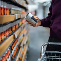 cropped shot of young woman pushing a shopping cart, grocery shopping in supermarket. she is holding a tin can and reading the nutritional label. routine grocery shopping. food shopping. making healthier food choices - junk f
