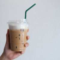 cropped shot view of someone hand holding a plastic cup of iced milk coffee against white wall. - junk food stock pictures, royalty-free photos & images