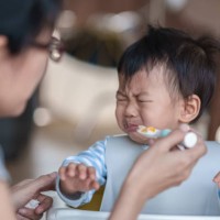 cute baby boy refusing to eat food and crying while his mother feeds him. - food stock pictures, royalty-free photos & images