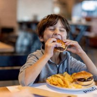 cute kid boy eats hamburger sitting in cafe. - junk food stock pictures, royalty-free photos & images