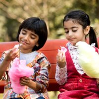 cute siblings eating cotton candies while sitting in park - junk food stock pictures, royalty-free photos & images