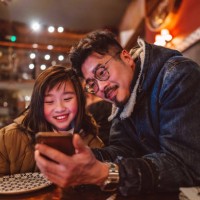 dad & daughter using smartphone in restaurant joyfully - food fotografías e imágenes de stock