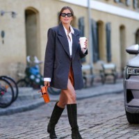Darja Barannik wears black cat eyes sunglasses, gold earrings, a gold large chain necklace, a white shirt, a dark gray long blazer jacket, camel...