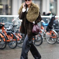 Darja Barannik wears sunglasses, a brown and khaki jacket with fluffy oversized parts at lapel and collar levels, a purple leather bag, black leather...