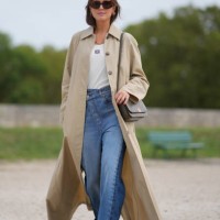Darja Barannik wears sunglasses, a white top, a beige long trench coat, blue denim jeans / pants, outside Loewe, during the Womenswear Spring/Summer...