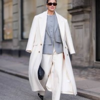 Darja Barannik wears sunglasses, golden earrings, a white oversized long coat, a gray oversized blazer jacket , white flared suit pants , pointed...