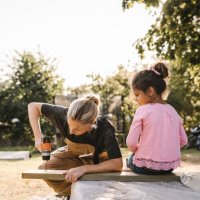 daughter looking at mother using drill machine on wooden plank in backyard - home decoration stock pictures, royalty-free photos & images