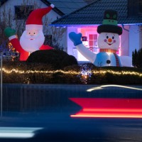 December 2022, Hessen, Frankfurt/Main: A giant illuminated Santa Claus and an equally large snowman stand in the front yard of a house decorated for...