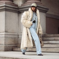 Deimante Kazenaite wears light blue jeans, matching denim shirt, light beige fur coat, beige bag and light pale green cap outside the MKDT fashion...