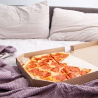 delicious delivered pizza in box on unmade bed in bedroom - junk food stock pictures, royalty-free photos & images