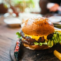 delicious double burger with french fries and vegetables on wooden cutting board - junk food stock pictures, royalty-free photos & images