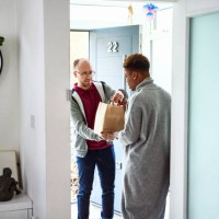 delivery man handing take away to woman at front door - junk food stock pictures, royalty-free photos & images