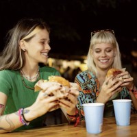 des femmes heureuses mangeant des hamburgers lors d’un festival de musique la nuit. - concert photos et images de collection