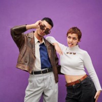 deux jeunes amis souriants prenant la pose devant un mur violet - fashion photos et images de collection