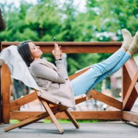 digital relaxation in glamping: brunette woman with feet up, surfing net and watching movies in phone, unwinds on log cabin patio - garden decoration stock pictures, royalty-free photos & images