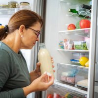 disgusted woman smelling expired milk by the fridge - food stock pictures, royalty-free photos & images