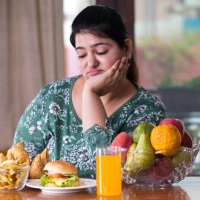 displeased woman with unhealthy and healthy food on table - junk food stock pictures, royalty-free photos & images