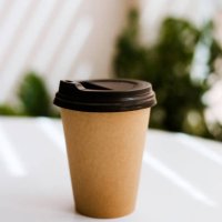 disposable coffee cup on table with plants on background. - junk food stock pictures, royalty-free photos & images