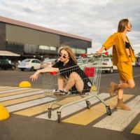 dos jóvenes rubias se divierten con el carrito de compras. mujer de moda - fashion fotografías e imágenes de stock