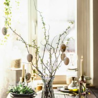 easter branches bunch with hanging easter eggs in glass vase on rustic wooden kitchen table with kitchen utensils, candle and decoration at window background - home decoration stock pictures, royalty-free photos & images