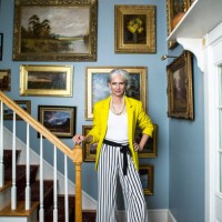 elegant woman in a fashionable outfit with grey hair standing in a staircase with oil paintings on the wall. - fashion stock pictures, royalty-free photos & images