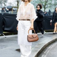 Elva Ni wears black sunglasses, a gold necklace, a white see-through long sleeved flower shirt, a white bra, a brown leather Gucci belt, a brown...