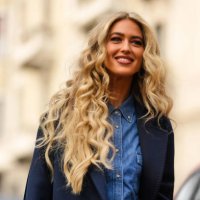 Emili Sindlev wears black leather and gold large earrings from Chanel, a navy blue wool long coat, a blue denim buttoned shirt / cargo pants...