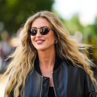 Emili Sindlev wears black sunglasses, a black shiny leather oversized bomber coat from Prada, a black shoulder-off cropped top, outside the Prada...