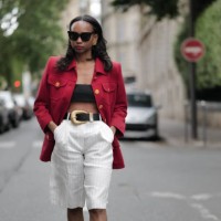 Emilie Joseph wears sunglasses, a red oversize blazer jacket with golden buttons, black bras / crop top, a black leather belt with large golden...