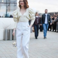 Emma Stone wears a a beige low-neck corset / top with ruffled puff oversized shoulder parts, high waist white flared pants, a cube-shaped bag,...