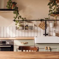 empty kitchen island with marble surface in foreground, green vintage countertop with drawers and pendant lights hanging above, lots of flowers in jars, blurred background - home decoration stock pictures, royalty-free photos
